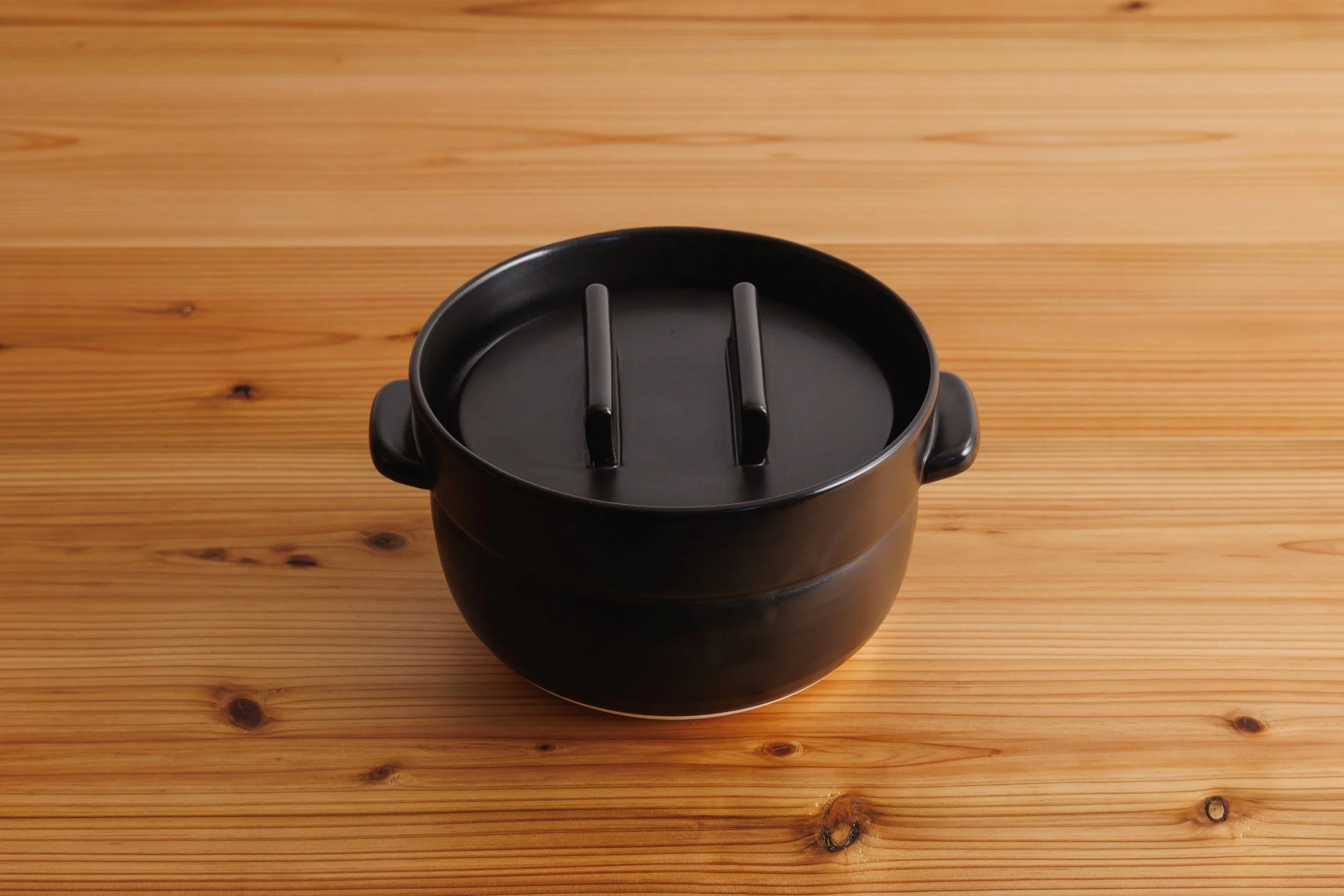 木のテーブルに置かれた、かもしか道具店の黒い炊飯土鍋「ごはんの鍋」