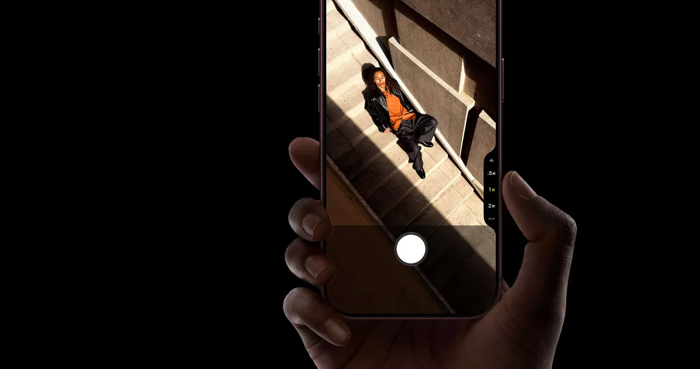 iPhone 18 Proを手に持ち、カメラアプリで階段に座る人物を撮影しようとしているApple公式画像