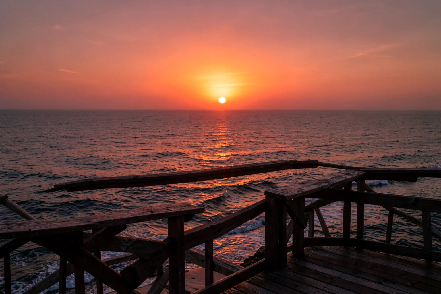 夕日に照らされた海辺の展望台から、オレンジ色に染まる海と空を眺める風景