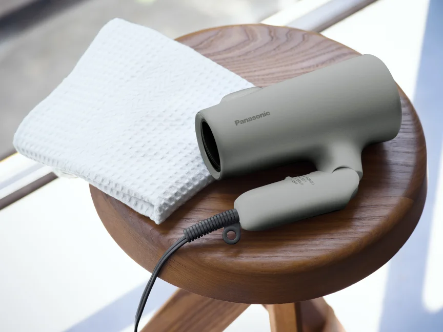 木製のスツールの上に白いタオルと並べて置かれた、ストーングレーのパナソニック イオニティ EH-NE5Pを写したパナソニック公式の画像