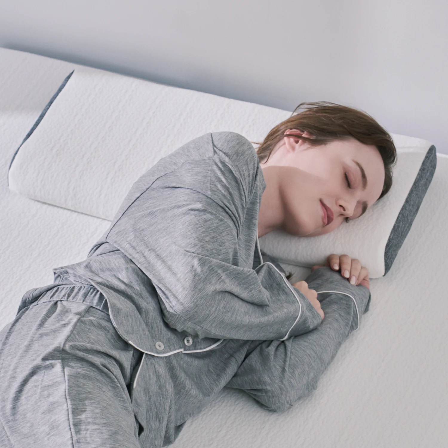 グレーのパジャマを着た女性がファセットピローに頭をのせて横向きで眠っている公式画像