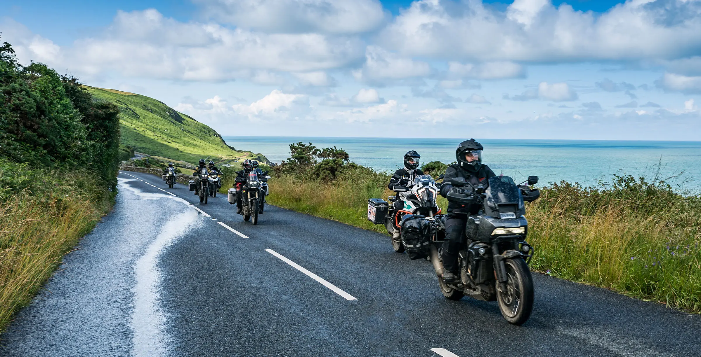 海沿いの道を複数台のバイクが連なって走るツーリングの様子を写したSENA公式のイメージ画像